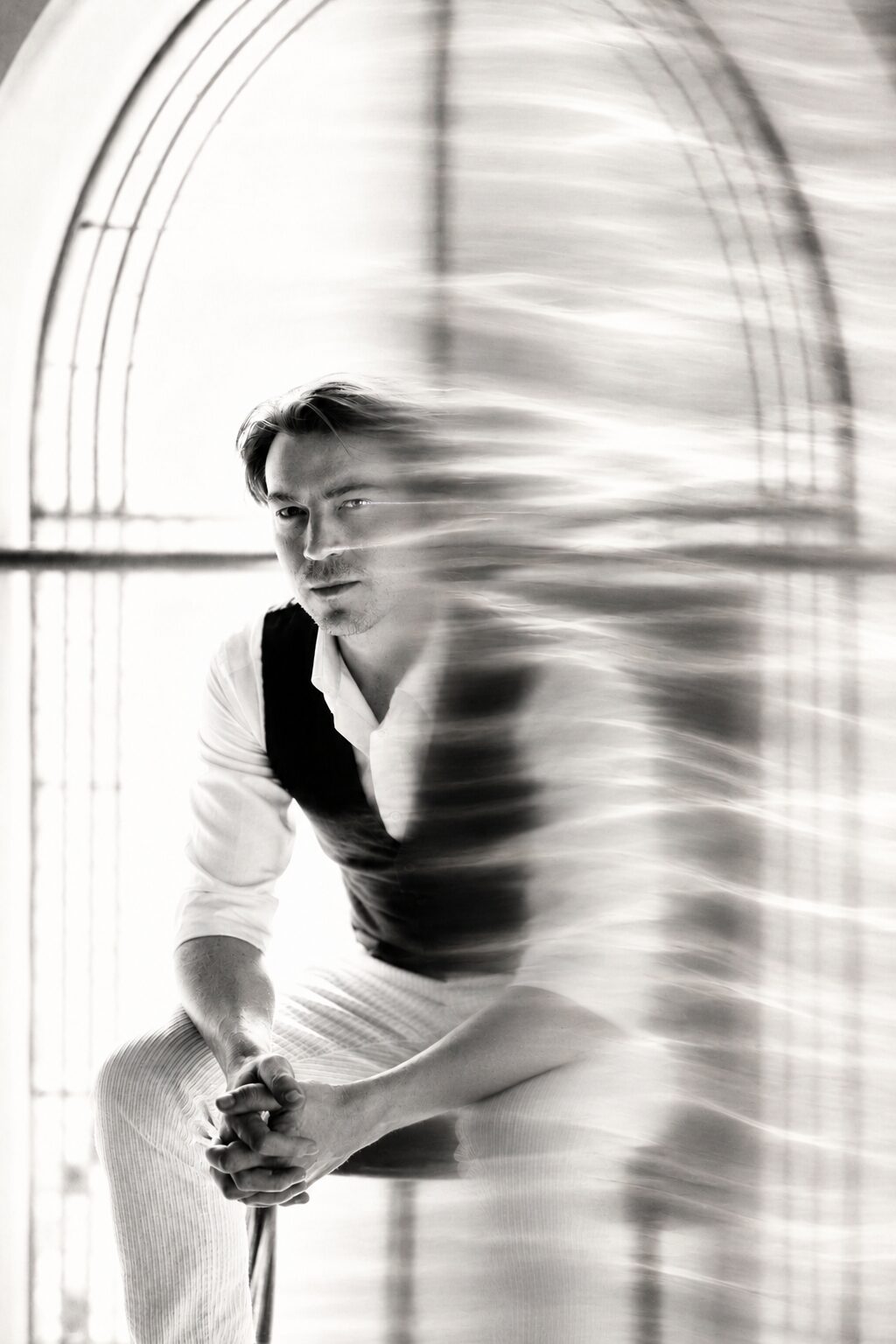 Portrait en noir et blanc de Stan Mosse, assis sous une grande verrière en arche